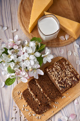 Dark multigrain bread made from rye, wheat, oats and barley with sunflower and flax seeds. Milk, cheese, apple tree flowers and light wooden rustic table.
