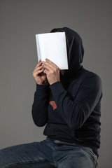 Happy world book and copyright day, read to become someone else - man covering face with book while reading on grey studio background. Celebrating, education, art, enjoying new characters concept.
