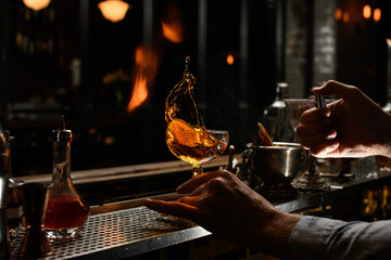 bartender holds by hand glass with splashed alcohol drink and spray to it.