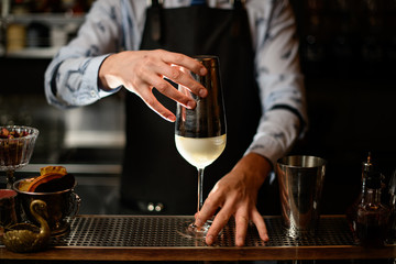 Fototapeta na wymiar Barman in black apron holds shaker over glass with cocktail.