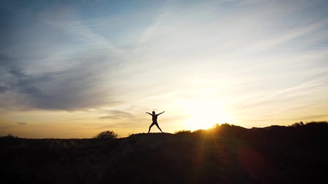 Silhouette of a woman practicing yoga in the dunes at sunrise