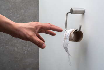 A hand reaching for an empty toilet paper holder (concept toilet paper finished)
