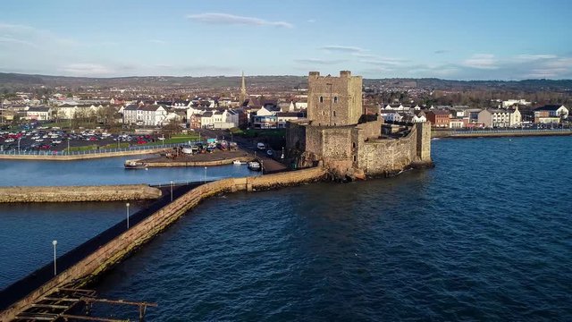 Medieval Norman Castle adn harbor in Carrickfergus near Belfast in sunrise light. Aerial 4K revealing video with marina, breakwater, yachts, parking lot and town 