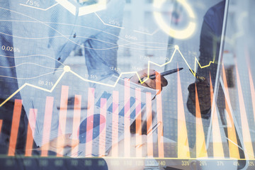 Double exposure of chart with businessman typing on computer in office on background. Concept of hard work.