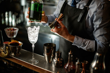 bartender in black apron begins to prepare green alcoholic cocktail