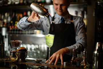 man at bar pours cocktail from shaker into glass.