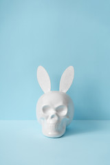 Skull with rabbit or bunny ears on pastel blue background. Creative minimal Easter concept. Hipster...
