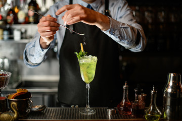 bartender carefully decorates by powder icy green cocktail in glass.