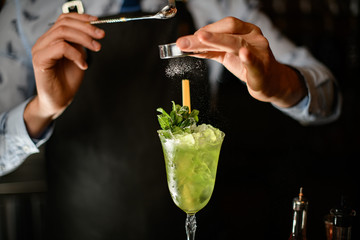 Professional bartender decorates by powder icy green cocktail in glass.