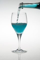 a bottle pouring blue liquor into a glass, isolated on white background