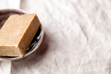 Hand made vegan natural soap bar with herbs and oat on textile background close-up. Spa organic treatments products. Horizontal orientation, copy space