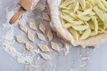 A homemade apple pie in the process of being made, with sliced granny smith apples in a pie plate, with fresh crust, next to a rolling pin on a floured pastry marble