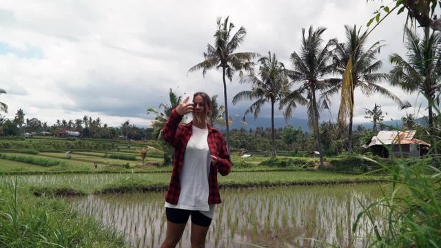 Happy woman walking and takes a video and photo on her phone in rice paddy enjoying vacation exploring exotic cultural landscape travel through bali indonesia