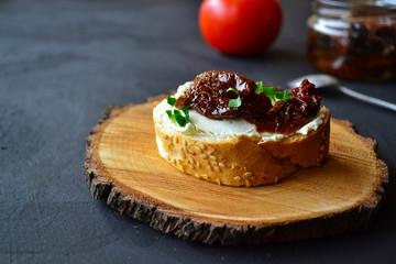 French baguette with cream cheese and dried tomatoes on a dark background.