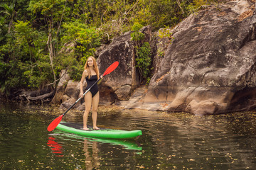 SUP Stand up paddle board woman paddle boarding on lake standing happy on paddleboard on blue water. Action Shot of Young Woman on Paddle Board - obrazy, fototapety, plakaty
