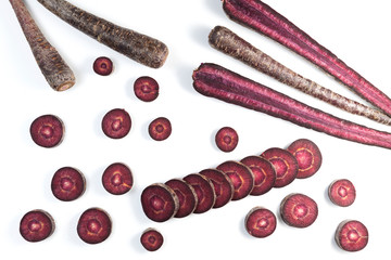 Unusual root vegetables. Purple carrots on light background. Vegetables whole and chopped. Copy space