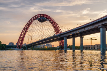 Fototapeta na wymiar Sunset view of Picturesque bridge with big red arch over the Moscow river, Moscow, Russian Federation.