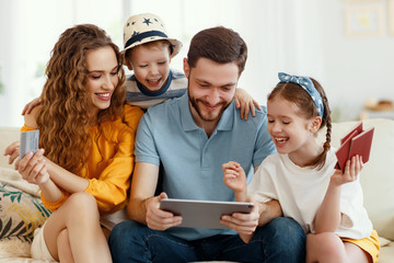 Smiling parents with kids gathering on sofa using tablet while picking tour online anticipating...