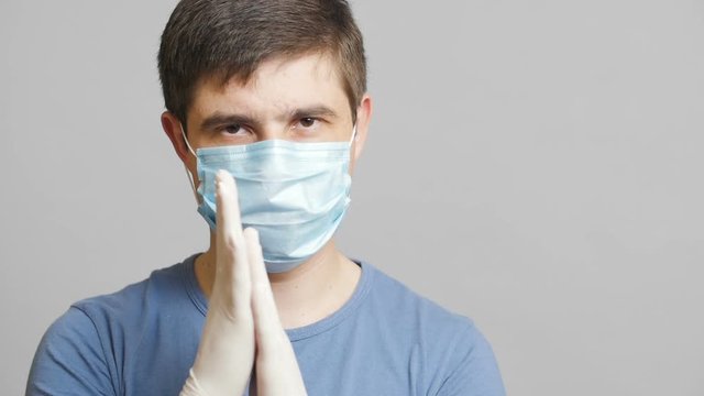 man with humor in surgical mask and sterile gloves on a gray background rubbing his hands slyly, concept medicine joke,strange doctor