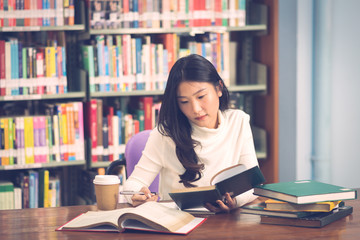 Young beautiful asian student girl working a book, learning in college library in university