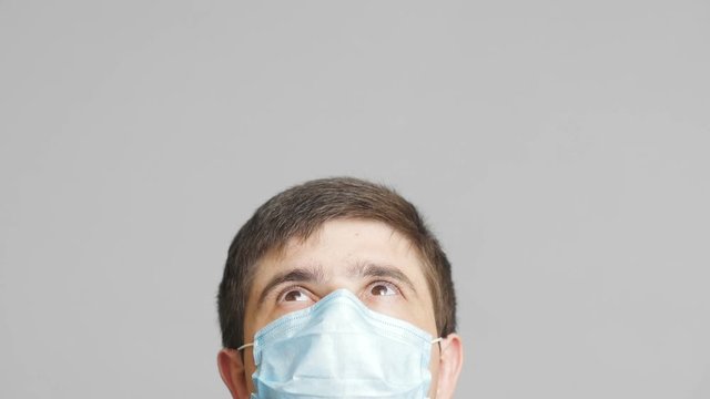 head of a young man in protective surgical mask looking up and watching news with eyes, concept of health and medicine,emotions of surprise and perplexity