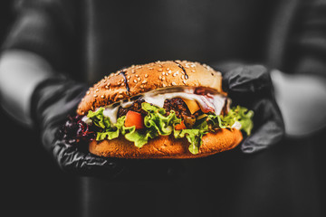 Color burger on a black and white photo. Bad food, fast-food. Burger in hands