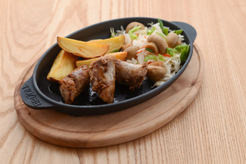 Grilled meat in mushroom's sauce and baked potato with cabbage mushroom salad in a pan on rustic wooden table.