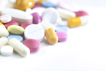 Multi-colored pills are scattered on the table. Pills of different sizes and purposes, small, large, white, pink, blue, yellow. For various illnesses, tablets lie as a backdrop with copy space.