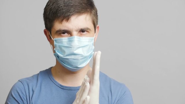 man with humor in surgical mask and sterile gloves on a gray background rubbing his hands slyly, concept medicine joke,strange doctor