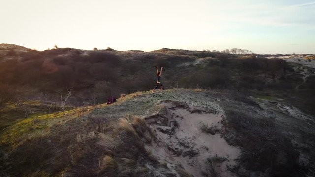 Silhouette of a woman practicing yoga in the dunes at sunrise. Drone shot. Aerial. 