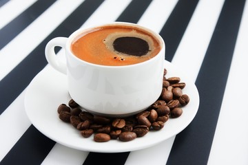White ceramic cup of strong coffee on striped background.