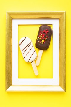 Dessert as Art. Brownie cake in form of popsicle in golden frame on yellow