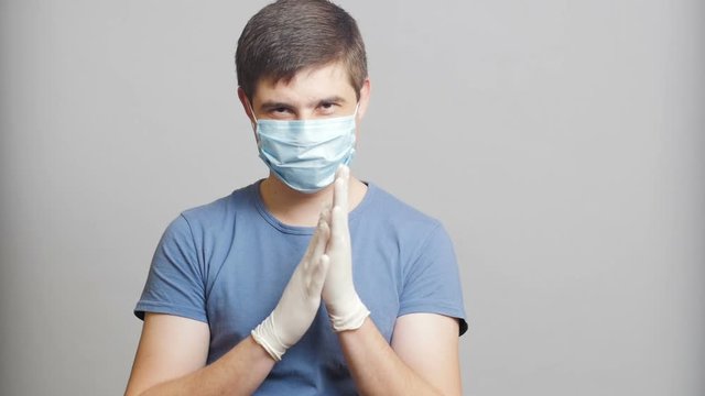man with humor in surgical mask and sterile gloves on a gray background rubbing his hands slyly, concept medicine joke,strange doctor