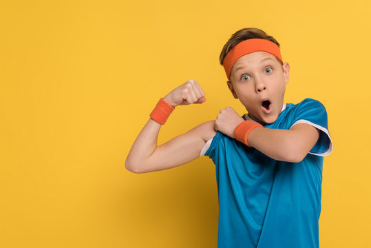 Shocked Kid In Sportswear Showing Muscles On Yellow Background