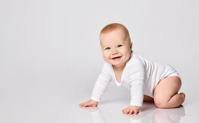 Chubby ginger baby boy in bodysuit, barefoot. He smiling, creeping on floor isolated on white...