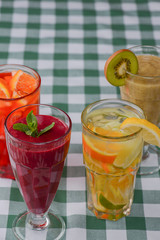 Four tropical mixed drinks, berries, orange and kiwi fruit cocktails served on green plaid tablecloth.