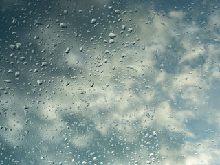 Wet window with rain drops and a cloudy sky outside.