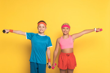 smiling kids in sportswear training with dumbbells on yellow background