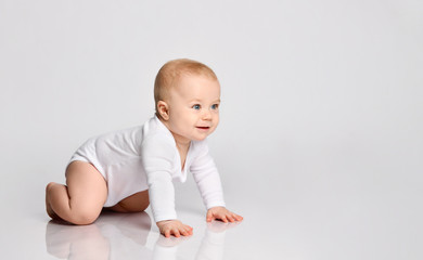 Fototapeta premium Chubby ginger baby boy in bodysuit, barefoot. He smiling, creeping on floor isolated on white background. Close up, copy space