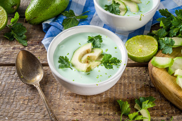 Homemade avocado cream soup with lime, herbs and avocado slices on wooden rustic background, copy space