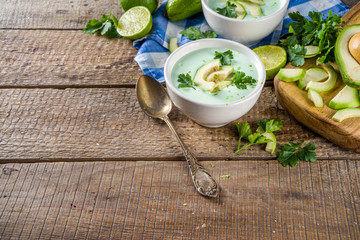 Homemade avocado cream soup with lime, herbs and avocado slices on wooden rustic background, copy space