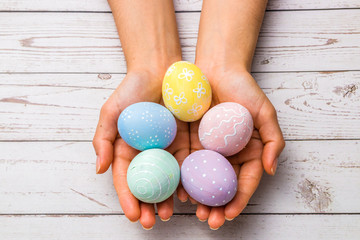 easter concept. closeup beautiful woman hands holding hand-painted easter eggs in tender pastel colors over wooden table