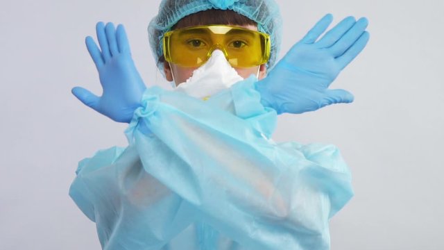 laborant in protection suit with blue gloves and yellow glasses showing stop sign with arms