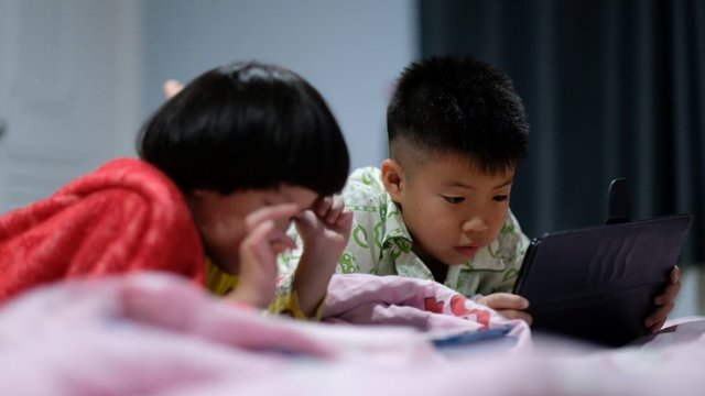 two chinese children addicted tablet, asian child watching tablet, kid use telephone together on their bed, play phone, kid addict smartphone