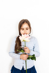 A girl of European appearance with long blond hair on a white background with a beautiful big pink rose, a girl with a gift of a flower, at home with mom and dad, a photo shoot for a child