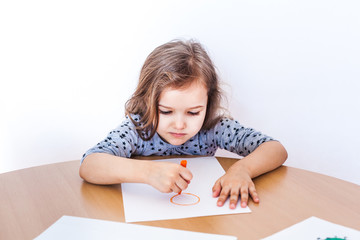 Naklejka premium A little girl in a dress sits at a table and draws, time at home with her family and mother, classes for the child, quarantine, time of illness, homework, child development, creativity