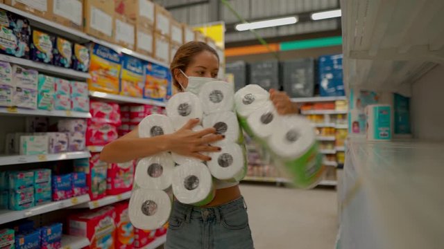 young woman wearing protect mask takes pack of toilet paper in shop with empty shelves