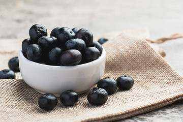 Fresh heap of blueberry in white clean bowl on sack cloth.