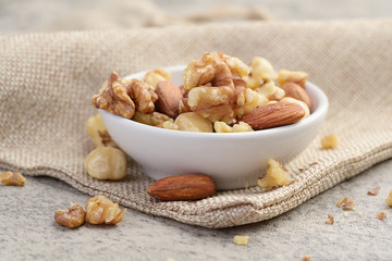 Mixed nuts in white clean bowl on sack cloth. Healthy food and snack concept.
