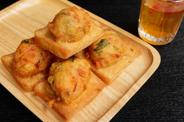 Fried Bread with Minced Pork Spread with sauce in a wooden dish on a black background. Close-up photo.